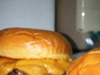 Dos hamburguesas dobles con queso fundido sobre una bandeja de acero.