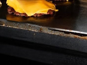 Una mano enguantada prensa las carnes sobre la plancha y coloca el queso encima.