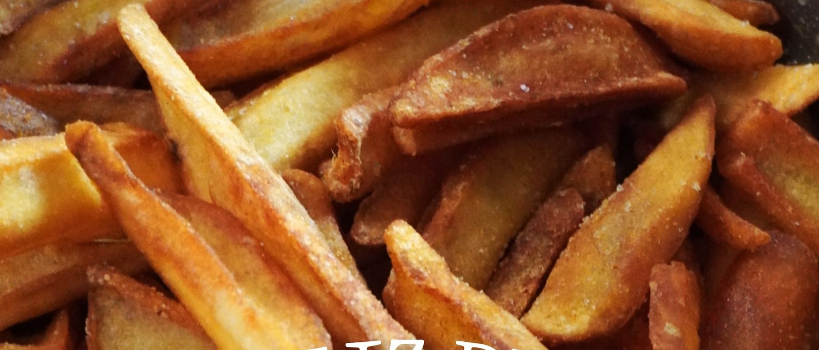Primer plano de patatas cortadas a mano recién fritas, doradas y con sal gruesa.